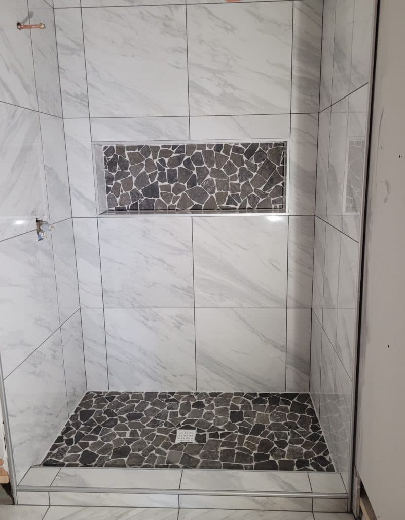 Marble-look tile shower with pebble floor and oversized niche